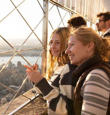 People looking out at NYC from the 86th floor observation deck at the Empire State Building Observatory.